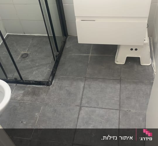 מקלחון עם דלת זכוכית ורצפת אריחים אפורה